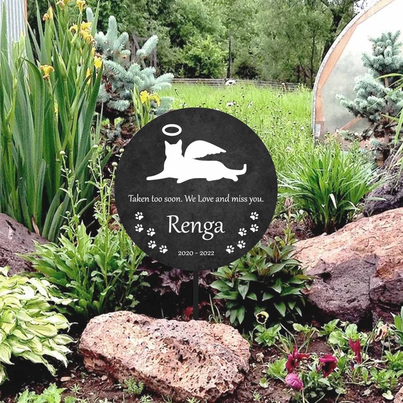 May include: Black memorial garden stake with a white silhouette of a cat with wings and a halo. The stake reads "Taken too soon. We Love and miss you. Renga 2020-2022" with paw prints around the text.