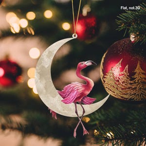 Könnte beinhalten: Ein rosafarbener Flamingo-Anhänger, der auf einem weißen Halbmond sitzt, eine skurrile Weihnachtsdekoration.
