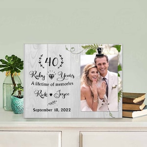 Könnte beinhalten: Ein weißer Holzrahmen mit einem Schwarzweißfoto eines Paares. Der Rahmen hat ein florales Design und den Text "40 Ruby Years A lifetime of memories Rick Joyce September 18, 2022".