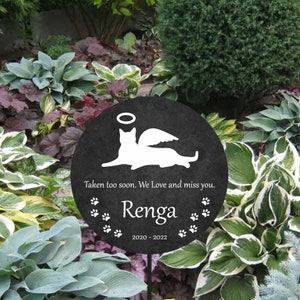 May include: Black memorial garden stake with a white silhouette of a cat with angel wings. The text reads "Taken too soon. We Love and miss you. Renga 2020 - 2022".