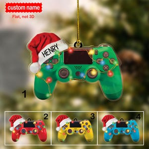 May include: A Christmas ornament shaped like a green video game controller with a red Santa hat on top. The controller has lights strung around it and the text "HENRY" is on the hat.