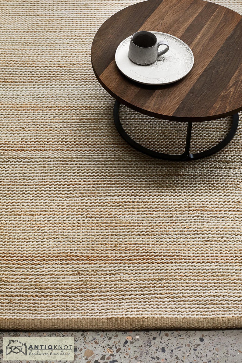 May include: A close-up of a natural fiber rug with a subtle ombre effect, transitioning from a light beige to a warm brown. The rug is woven with a textured, slightly raised pattern. A wooden coffee table with a black metal base sits on top of the rug.