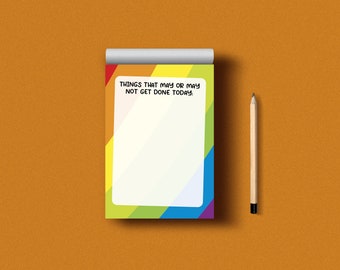 Puede incluir: Un bloc de notas con rayas de arcoíris con el texto "Things that may or may not get done today." El bloc de notas está sobre una superficie marrón con un lápiz al lado.