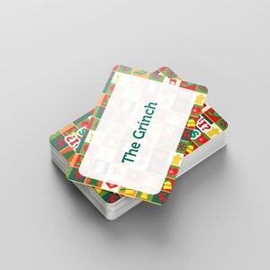 Puede incluir: Una pila de cartas de juego con tem&aacute;tica navide&ntilde;a con un borde verde, rojo y amarillo. La carta superior tiene un rect&aacute;ngulo blanco con el texto "The Grinch" en verde.