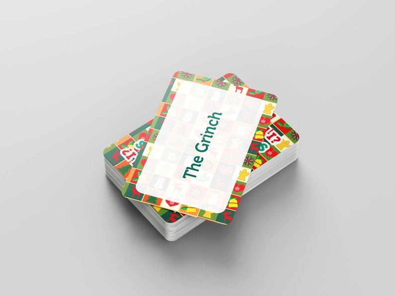 Puede incluir: Una pila de cartas de juego con tem&aacute;tica navide&ntilde;a con un borde verde, rojo y amarillo. La carta superior tiene un rect&aacute;ngulo blanco con el texto "The Grinch" en verde.