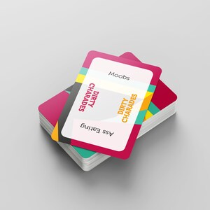May include: A stack of playing cards with a pink and white design. The top card has the words "Moobs", "Dirty Charades", and "Ass Eating" printed on it. The cards have a colorful geometric design on the edges.
