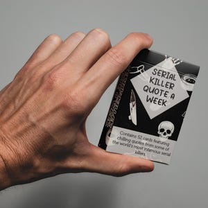 Può includere: Un mazzo di carte in bianco e nero intitolato "SERIAL KILLER QUOTE A WEEK" è tenuto in mano. Il mazzo presenta illustrazioni di un coltello, un teschio e altre grafiche. Il testo dice che contiene 52 carte con citazioni.