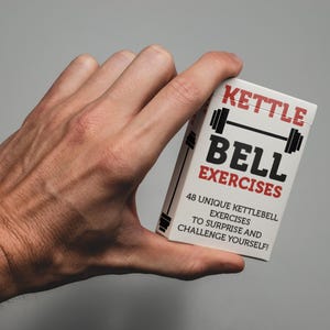 May include: A white box with the words "Kettle Bell Exercises" in black and red, with a barbell graphic. The box also states "48 Unique Kettlebell Exercises to Surprise and Challenge Yourself!"