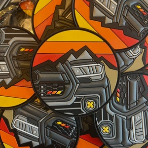 May include: Close-up of a stack of round, colorful patches featuring a black and gray car grille with yellow accents. The patches have a retro-inspired design with orange, yellow, and red stripes.