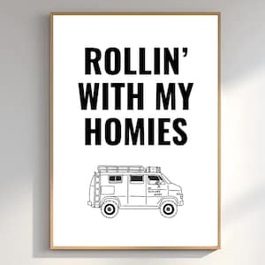 May include: A framed print with the text "ROLLIN' WITH MY HOMIES" in bold black letters above a black and white illustration of a van. The van has a roof rack and the words "EXPLORE MORE" on the side.