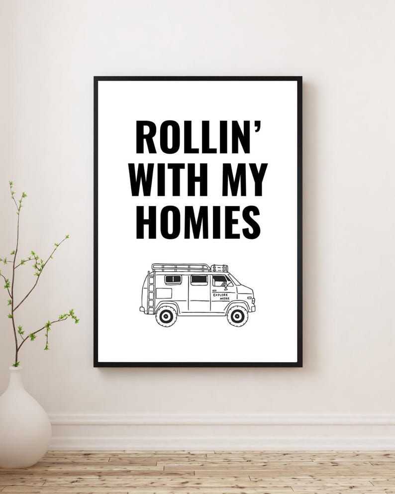 May include: Black framed print with the text "ROLLIN' WITH MY HOMIES" above a line drawing of a van. The van has a roof rack and the words "EXPLORE MORE" on the side. The print is displayed on a white wall.