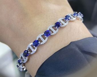 May include: A silver bracelet with a chain design featuring oval-shaped blue gemstones surrounded by smaller clear gemstones.