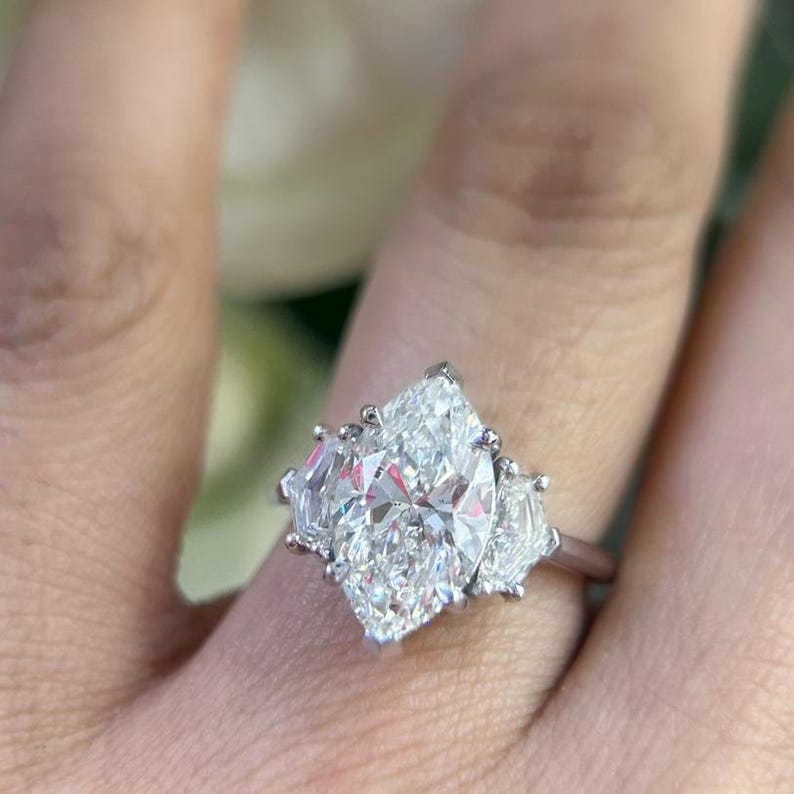 May include: A silver ring with a large, clear, oval-shaped diamond in the center. The diamond is surrounded by three smaller, clear, pear-shaped diamonds.