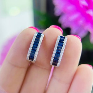 May include: A pair of silver hoop earrings with a row of blue sapphire stones and a row of clear diamonds.