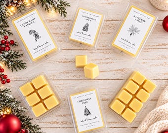 May include: Four clear plastic clamshell containers of yellow beeswax melts with white labels featuring black text and illustrations. Scents include Candy Cane Vanilla, Gingerbread Spice, Bayberry + Pine, and Christmas Tree. Each label states 2 oz / 57 g.