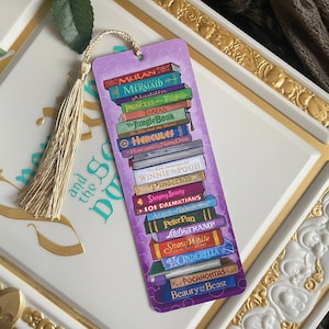 May include: A purple bookmark featuring a stack of colorful books with titles like "Mulan," "The Little Mermaid," and "Beauty and the Beast." A gold tassel hangs from the top. The bookmark is set against a decorative white background.
