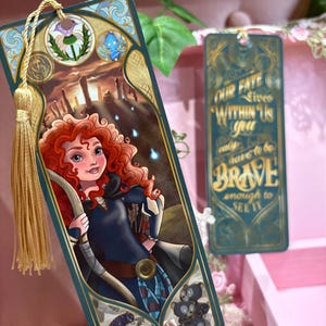 May include: Two decorative bookmarks. One features a red-haired character with a bow and arrow, set against a landscape. The other bookmark is teal with the text "OUR FATE LIVES WITHIN US YOU only have to be BRAVE enough to SEE IT."