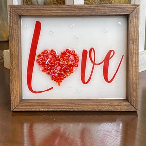 May include: A framed sign with the word "LOVE" in red lettering. A red heart made of beads is in the center of the word.