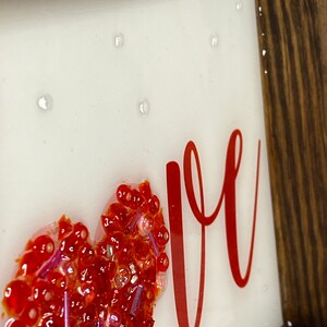 May include: A framed piece of art with a red heart made of glitter and the word "love" written in red cursive.