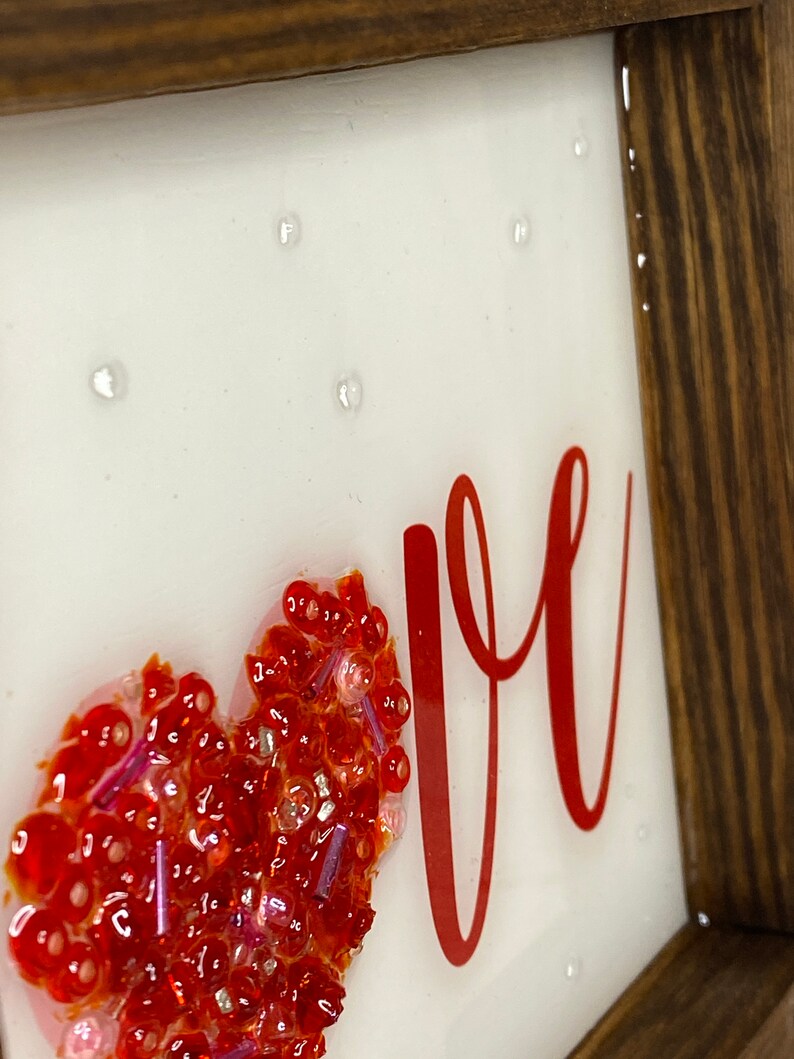 May include: A framed piece of art with a red heart made of glitter and the word "love" written in red cursive.