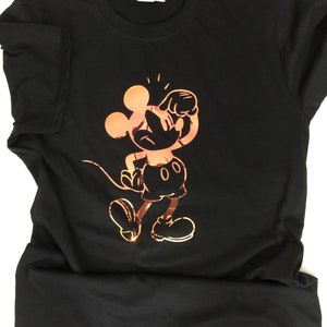 May include: Black t-shirt featuring a copper-colored graphic of Mickey Mouse in a playful pose. The design is a stylized illustration of the iconic cartoon character. The shirt is made of a soft material and has a crew neck.