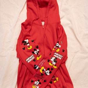 May include: Red zip-up hoodie with Mickey Mouse graphics on the sleeves and the text "Mickey Mouse" on the left and right sleeves.