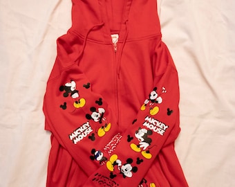 Puede incluir: Sudadera roja con cremallera y capucha con gráficos de Mickey Mouse en las mangas y el texto "Mickey Mouse" en las mangas izquierda y derecha.