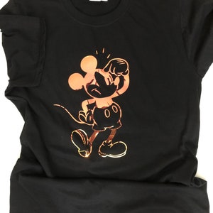 以下が含まれることがあります： 黒いTシャツ。銅色のミッキーマウスのグラフィックが特徴で、クラシックなポーズをとっています。このデザインは、象徴的な漫画のキャラクターの様式化されたイラストです。このシャツはクルーネックと半袖で、カジュアルウェアに適しています。