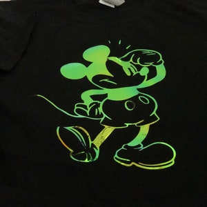 以下が含まれることがあります： 黒いTシャツ。緑と黄色のグラデーションでミッキーマウスが描かれています。漫画のキャラクターは走っているポーズで描かれています。Tシャツはクルーネックです。