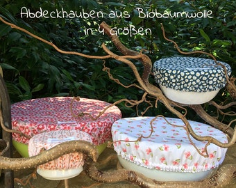 May include: Four elasticized fabric bowl covers in various sizes and patterns, including red floral, pink berry, and white daisy prints. The text Abdeckhauben aus Biobaumwolle in 4 Größen is visible above the covers.