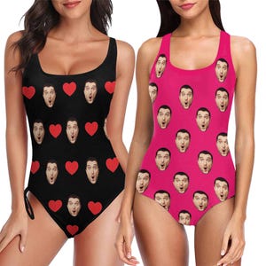 May include: Two women wearing one-piece swimsuits with a pattern of red hearts and a man's face. The swimsuits are black and pink.