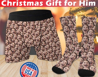 May include: A pair of black and white socks with a pattern of faces. The socks are on a wooden surface. There is a pair of boxer shorts with a similar pattern of faces. The boxer shorts are on a wooden surface. The boxer shorts have a black waistband. There is a red, white, and blue sticker that says "Made in USA" on the wooden surface.
