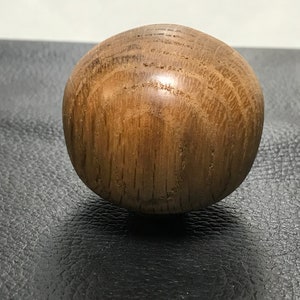 Può includere: Un oggetto sferico in legno con una finitura liscia e lucida. La superficie presenta un colore marrone chiaro naturale con venature scure visibili che corrono verticalmente sulla forma arrotondata, evidenziando la consistenza organica del legno.