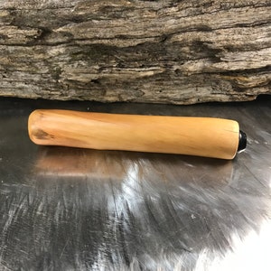 May include: A cylindrical wooden handle with a smooth, light tan finish and natural grain patterns. The handle features a rounded end and a small, dark-colored circular component at the opposite end, showcasing a polished, organic wood texture.