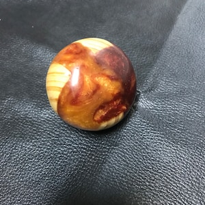 May include: A spherical object crafted from a combination of light-colored wood with visible grain patterns and a polished, swirling amber and deep reddish-brown resin inlay that creates a smooth, glossy, and rounded surface texture.