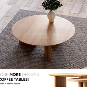 May include: A round wooden coffee table with three legs sits on a gray rug. A white vase with green foliage is on the table. The text "EXPLORE MORE DESIGNS OF COFFEE TABLES!" is at the bottom of the image.
