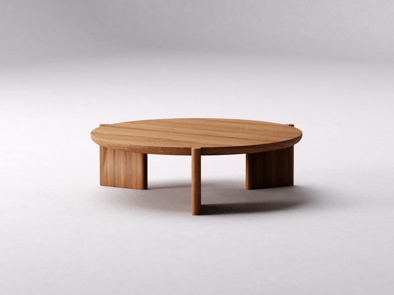 May include: A round wooden coffee table with a natural wood finish and four legs. The table has a simple, modern design.