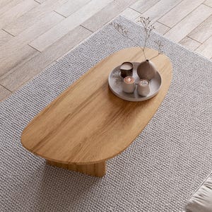 Puede incluir: Una mesa de centro ovalada de madera marr&oacute;n claro sobre una alfombra gris claro. La mesa tiene una bandeja decorativa con un jarr&oacute;n peque&ntilde;o, dos velas y dos tazas peque&ntilde;as. La alfombra est&aacute; sobre un suelo de madera marr&oacute;n claro.
