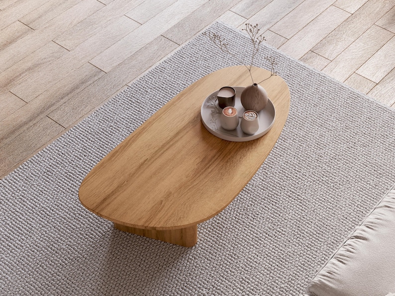 Puede incluir: Una mesa de centro ovalada de madera marr&oacute;n claro sobre una alfombra gris claro. La mesa tiene una bandeja decorativa con un jarr&oacute;n peque&ntilde;o, dos velas y dos tazas peque&ntilde;as. La alfombra est&aacute; sobre un suelo de madera marr&oacute;n claro.