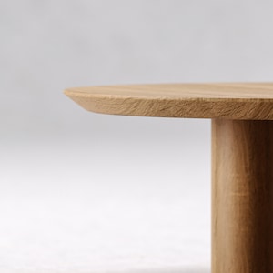 May include: Close-up of a light brown wooden table. The table has a round top and two cylindrical legs. The wood grain is visible on the surface. The table is a natural wood color.