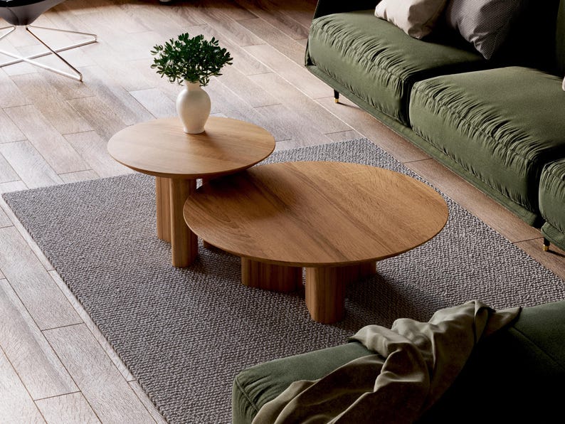 Puede incluir: Dos mesas de centro redondas de madera con un acabado de madera natural. La mesa m&aacute;s grande est&aacute; encima de la m&aacute;s peque&ntilde;a. Las mesas est&aacute;n sobre una alfombra gris delante de un sof&aacute; verde.