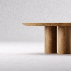 May include: A light brown wooden coffee table with a rectangular top and three cylindrical legs. The table is made of solid wood and has a natural finish. The design is minimalist and modern.