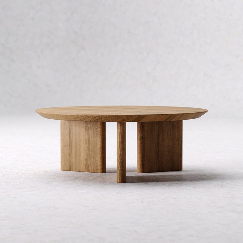 May include: A light brown, oval-shaped coffee table. The table is made of wood and has a simple, modern design. The table is supported by two rectangular legs and a single vertical support, creating a minimalist aesthetic.