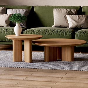 May include: Two wooden coffee tables with rounded tops and a natural wood finish. The larger table is in front of a green sofa with white and beige pillows. A small potted plant sits on the smaller table.