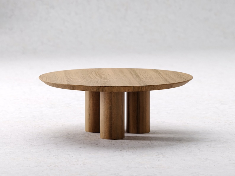 May include: A round wooden coffee table with a light brown finish. The table has a circular top supported by three cylindrical legs. The design is minimalist and modern, suitable for living rooms or lounges.