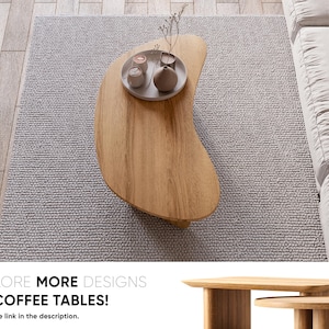 May include: A light brown, organically shaped wooden coffee table with a tray of decorative items. The table sits on a grey rug, near a white sofa. The image includes the text "EXPLORE MORE DESIGNS OF COFFEE TABLES!"