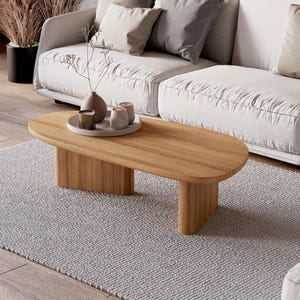 Puede incluir: Una mesa de centro ovalada de madera clara, sobre una alfombra gris clara, con un sof&aacute; blanco al fondo. La mesa tiene una veta de madera natural y un dise&ntilde;o minimalista. Objetos decorativos sobre una bandeja.