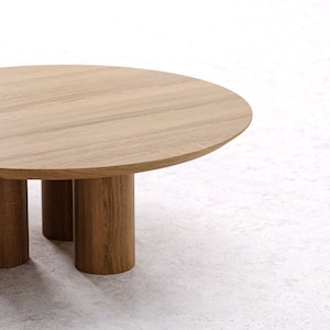 May include: A round wooden coffee table with a light brown finish. The table has a circular top and is supported by three cylindrical legs. The table is approximately 30 inches in diameter.