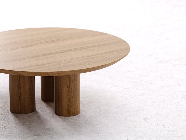 May include: A round wooden coffee table with a light brown finish. The table has a circular top and is supported by three cylindrical legs. The table is approximately 30 inches in diameter.