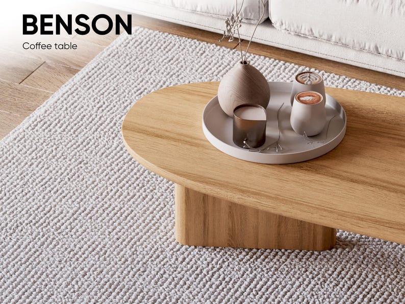 Puede incluir: Una mesa de centro de madera clara con bordes redondeados y una base s&oacute;lida. Una bandeja blanca sobre la mesa contiene un jarr&oacute;n, dos tazas peque&ntilde;as y una vela. El texto "BENSON Coffee table" est&aacute; en la esquina superior izquierda.